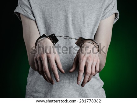 Prison and convicted topic: man with handcuffs on his hands in a gray T-shirt and blue jeans on a dark green background in the studio, put handcuffs on the drug dealer