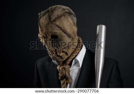 Fear and Halloween theme: a brutal killer in a mask holding a bat on a dark background in the studio