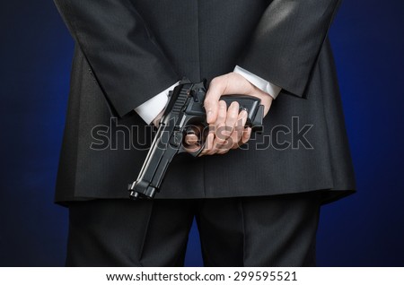 Firearms and security topic: a man in a black suit holding a gun on a dark blue background in studio isolated