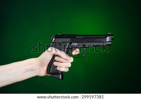 Firearms and murderer topic: human hand holding a gun on a dark green background isolated in studio