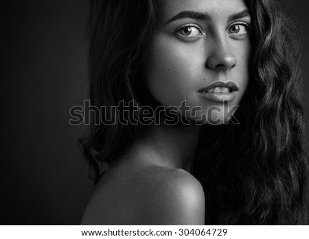 Dramatic portrait of a girl theme: Black and white portrait of a young beautiful girl on a dark background in the studio