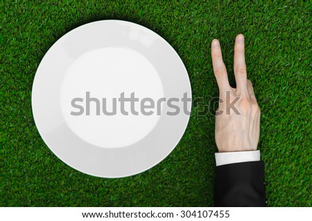 Business lunch and fresh fruit and vegetables on the nature theme: the human hand in black suit shows on the plate on a background of green grass top view