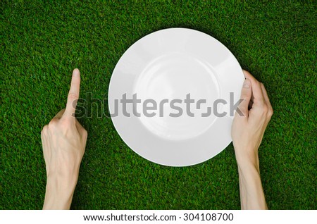 Restaurant and fresh fruit and vegetables on the nature theme: the human hand shows the plate on a background of green grass top view