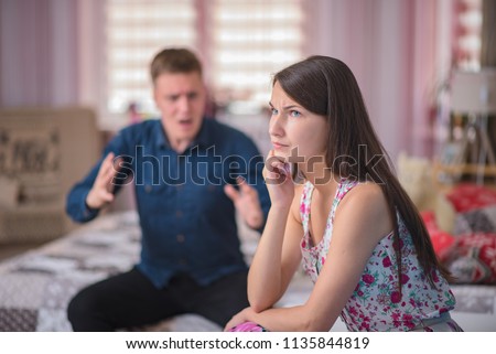 family relations, problems, difficulties, the dispute of young husband and wife on the sofa in the bedroom. The husband and wife are sitting right in front of the camera and look unhappy