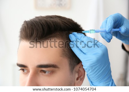 Young man with hair loss problem receiving injection on blurred background, closeup