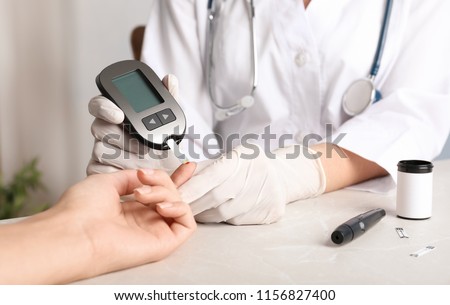 Doctor checking blood sugar level with glucometer at table. Diabetes test