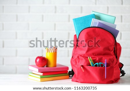 Backpack with school stationery on table against brick wall