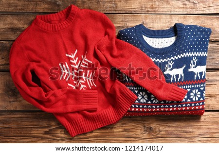 Christmas sweaters with pattern on wooden background, top view