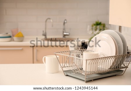 Dish drainer with clean dinnerware on table in kitchen. Space for text