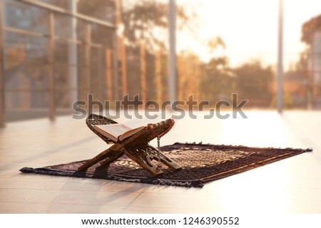 Rehal with open Quran and Muslim prayer beads on rug indoors. Space for text