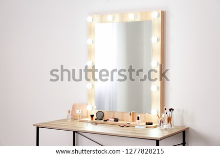 Table with makeup products and mirror near white wall, space for text. Dressing room interior