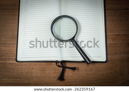 Opened blank notebook with Magnifying Glass on wooden background