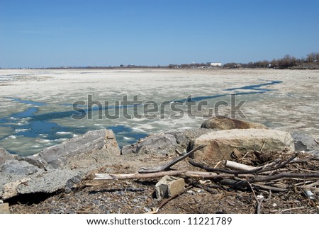Ice melting near Lake Erie shoreline at beginning of spring thaw. Shot near Buffalo NY USA. Rocks, debris, and driftwood in foreground.