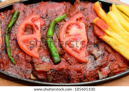 Traditional Turkish Bursa iskender kebap doner served with special red sauce and yogurt in the middle, garnished with grilled tomatoes and peppers