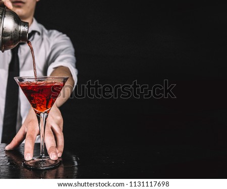 Expert barman making cocktail at nightclub.  Bartender preparing red cocktail at cocktail glass at the bar. Preparing of cosmopolitan cocktail. Red alcoholic drink in glasses on bar.