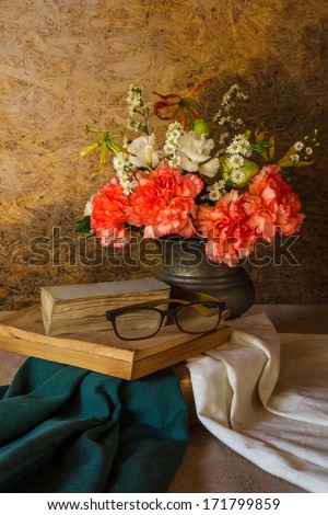 Still life with glasses resting on a book and a flower in a vase.