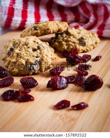 Oatmeal cranberry cookies on a wooden surface with dried cranberries and a red and white towel to accent.