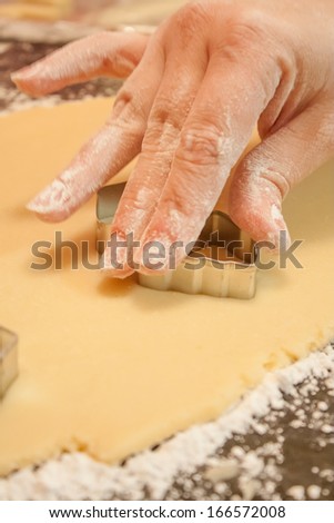 A woman\'s hand using a metal cookie cutter to cut shapes out of rolled out dough.