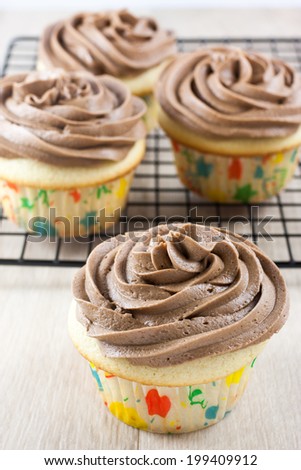 Chocolate frosted cupcakes sitting on a baking rack on a wooden table.