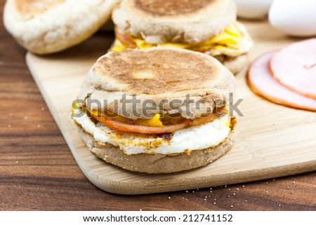 English muffin, egg, ham, and cheese breakfast sandwich on a cutting board with ingredients in the background.