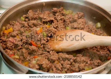 Fresh ground beef and vegetables cooking in a skillet with a wooden spoon stirring it.