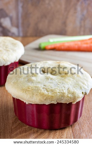 Chicken pot pie in a red ramakin cools on a wooden counter top in the afternoon sun.
