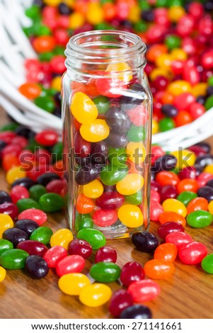 Jelly beans in a glass jar with a spilled basket of jelly beans behind it.