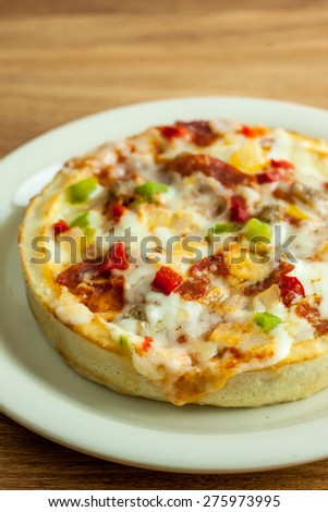 A personal sized deep dish pizza on a white plate, sitting on a wooden table.