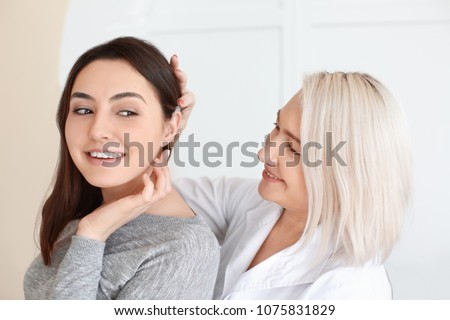 Otolaryngologist putting hearing aid in woman\'s ear on light background