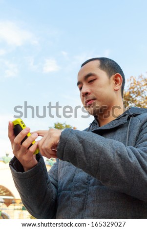 handsome thai man with gray coat is playing mobile phone