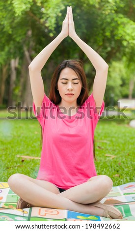 Young asian woman in pink sitting on grass and practicing yoga