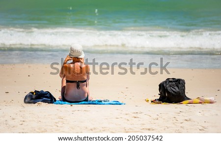 elderly bikini woman sitting in the sand on the beach and looks into the distance the sea horizon