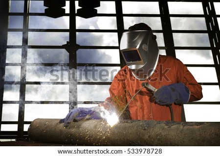 Industrial welder working a welding metal with protective mask and sparks on piping work