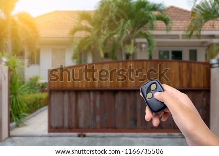 Female hand showing and using remote control to open or close the automatic wooden gate with home blurred background. Security and save time concept.