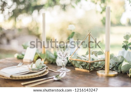 Luxury wedding reception dinning table setup with eucalyptus branches and gold geometric decoration on a rustic wooden table