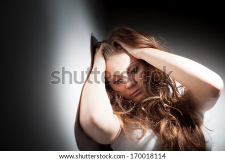 Young woman suffering from a severe depression, anxiety (very harsh lighting is used on this shot to underline the gloomy mood of the scene, color toned image)