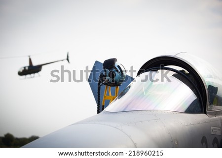 Detail of military fighter/interceptor/jetplane cockpit with pilot\'s oxygen mask and helmet, ready to take off in case of terrorist attack (helicopter in background, colorful image)