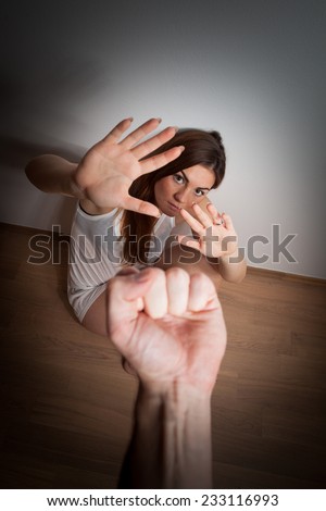 Woman/girl covering her face in fear of domestic abuse/violence sitting on the floor, punch against her face (very harsh light for underline the atmosphere, color toned image)