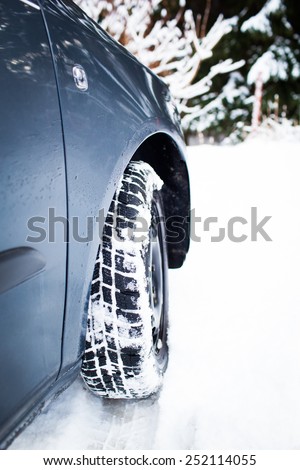 Winter driving conditions. Snow storm, snow tires, snow chain, driving hazards and cold weather concept (colorful image, close-up image of front wheel of stuck car, focused on tire)