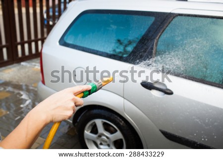 Young woman hand washing her silver family car in a front yard
