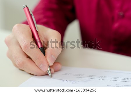 Signing a contract by the red ballpoint with shallow focus on signature.
