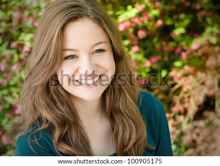 Close up Portrait of One Beautiful and Cheerful Young Lady in a Teal Blouse, Happy Outside in the Spring Garden Setting with Space for Copy or Text.