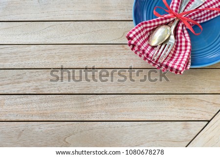 A Red White and Blue Picnic Table Place Setting with napkin, fork and spoon and plate in an upper corner on horizontal \
wood board table top background with room or space for copy, text or your words.