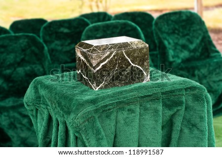 A Funeral Service Scene with a Marble or Granite Urn placed on a Table in front of chairs outside at the gravesite.