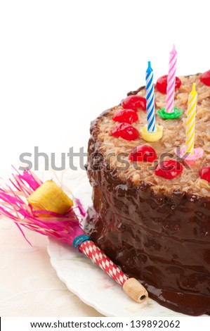 Closeup of a German Chocolate Birthday cake with chocolate frosting, maraschino cherries, vintage candle holders and party blower for children, kids, or adults on white background with room for text