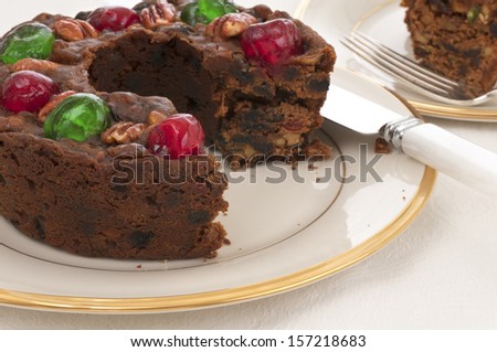 Christmas Fruit Cake with red and green cherries on top on a China Plate on a Table with a White Table Cloth