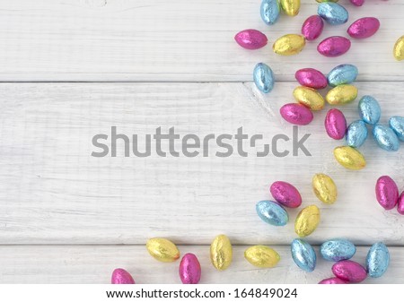 Colorful Wrapped Chocolate Easter Eggs Scattered On White Board Background With Room Or Space For Text, Copy Or Words. Horizontal