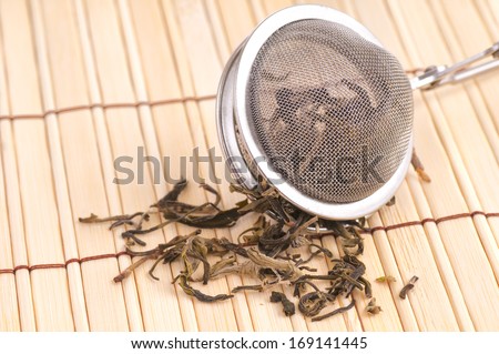 Black Loose Tea Falling out of a Tea Strainer on a Bamboo Mat, drank with water for pleasure and as disease prevention
