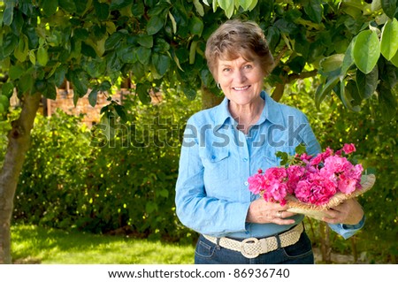 Smiling and Pretty Senior Woman Enjoying Her Garden and Holding a Bouquet of Pink or Red Roses that She Just Picked