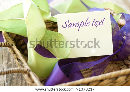 Brown Woven Basket Filled with Green and Purple Ribbons and a Plain White Paper with Room or Space for Text, Copy or your words.  Horizontal, closeup looking down above view.